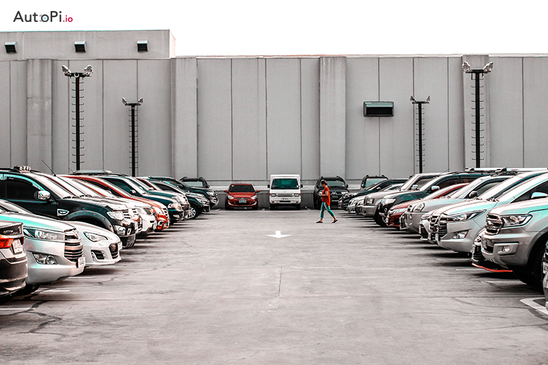 A parking lot with a woman crossing through the middle and cars parked on the sides