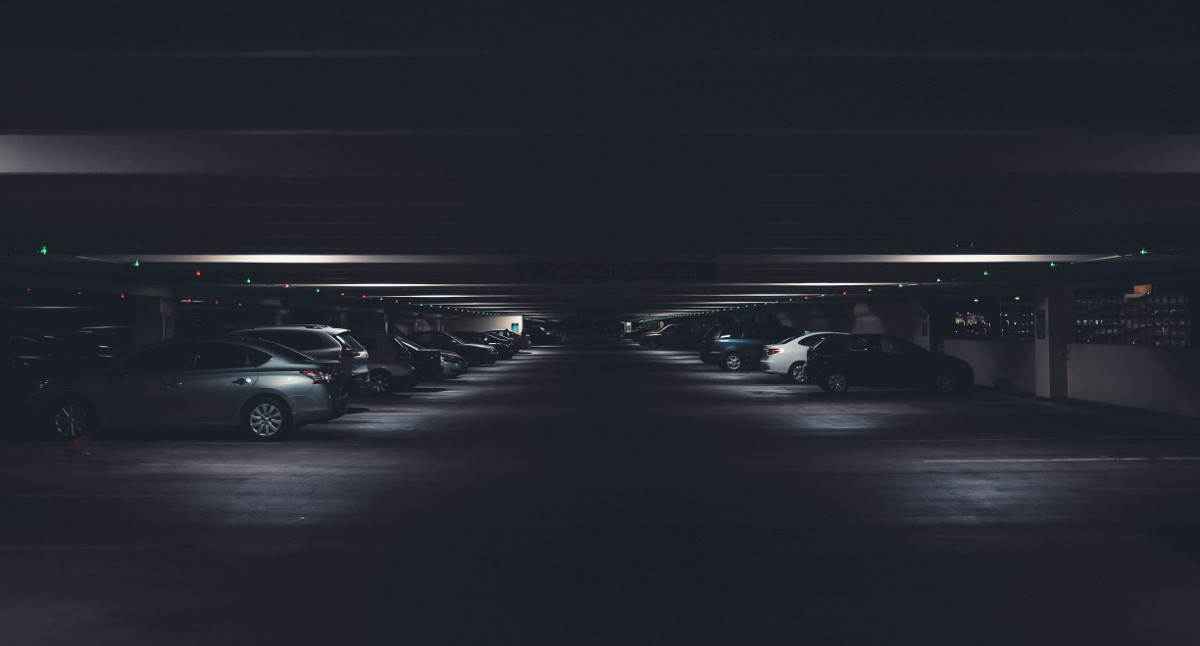 A dark picture of an underground parking lot with cars on a side and a bit of light in the middle